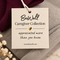 Cream-colored product tag with gold heart and burgundy ribbon attached to gray fabric with dried flowers.