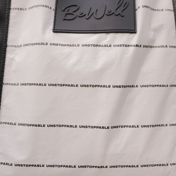 White tote bag with repeated "UNSTOPPABLE" text pattern and gray woven label at top.