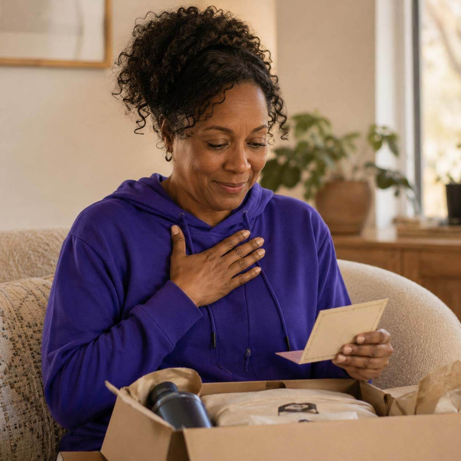 Woman in purple hoodie opening a cardboard box at home, smiling while holding product documentation.