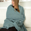 Woman wrapped in a teal, textured blanket, sitting on a cream couch.