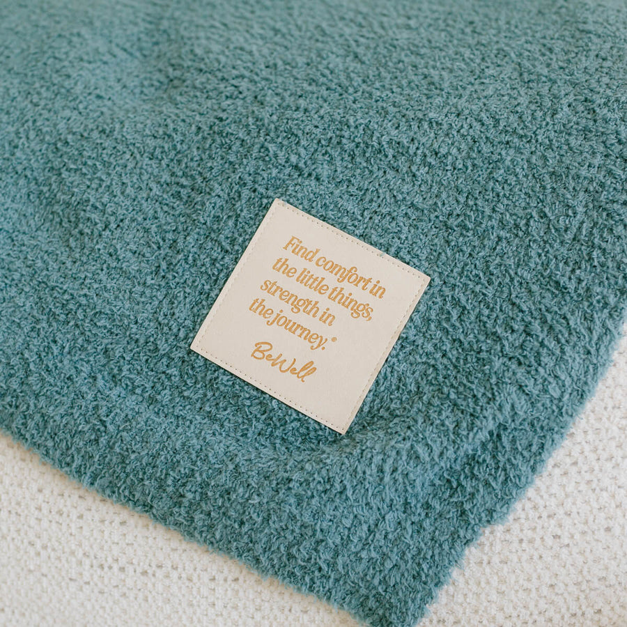 Close-up of teal infusion blanket with inspirational message label on soft fabric.