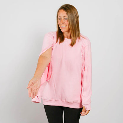 Woman wearing a pink crewneck sweatshirt over black pants, smiling while looking down.