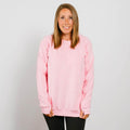 Woman wearing a pink crewneck sweatshirt and black pants, smiling at camera.