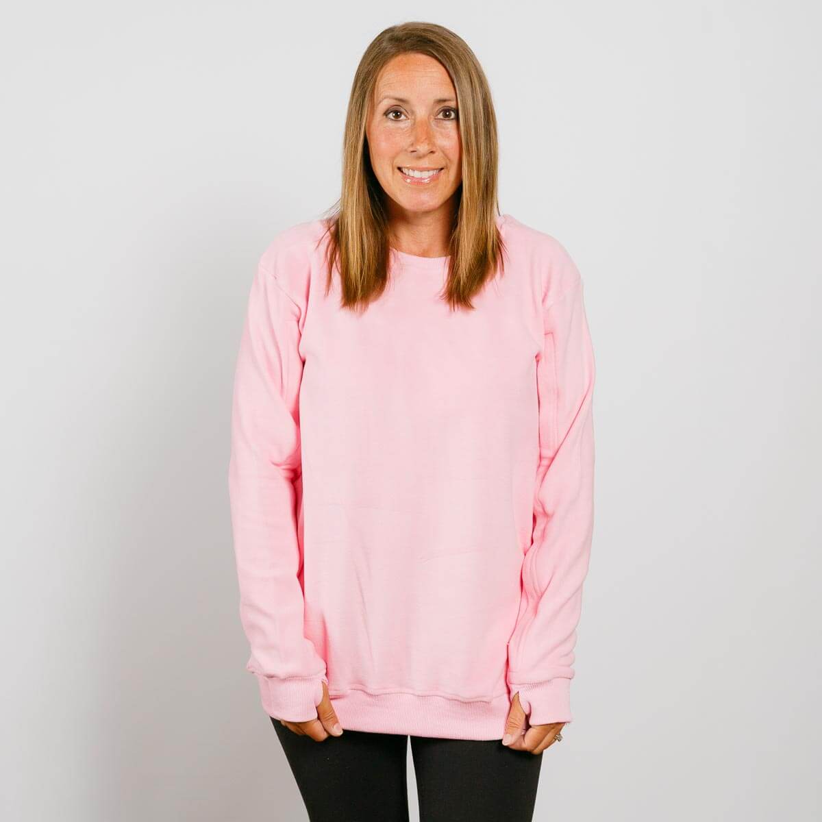 Woman wearing a pink crewneck sweatshirt and black pants, smiling at camera.