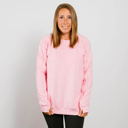 Woman wearing a pink crewneck sweatshirt and black pants, smiling at camera.