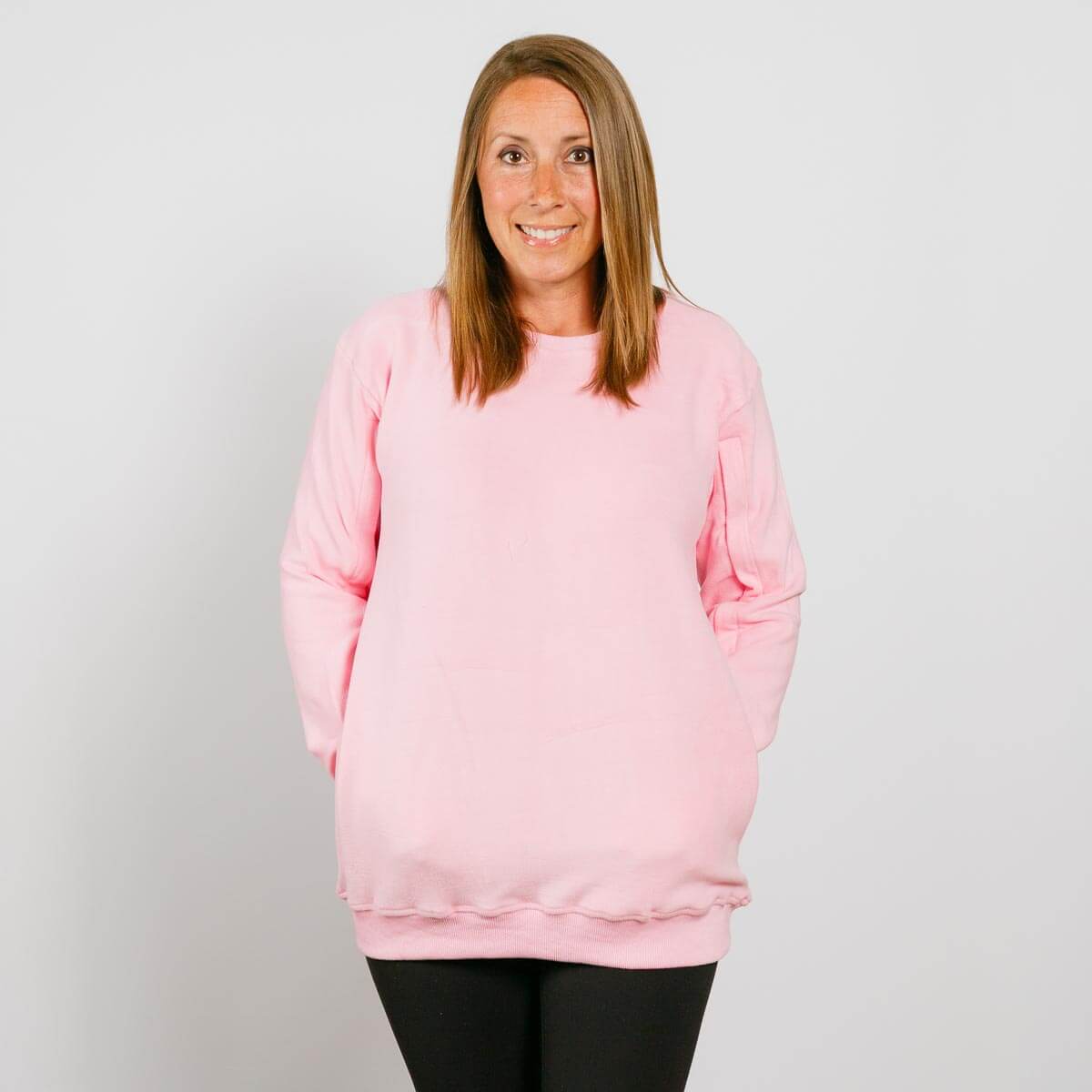 Woman wearing a pink crewneck sweatshirt and black pants, smiling at camera against white background.