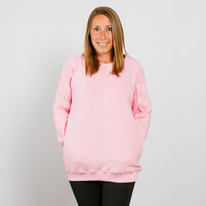 Woman wearing a pink crewneck sweatshirt and black pants, smiling at camera against white background.