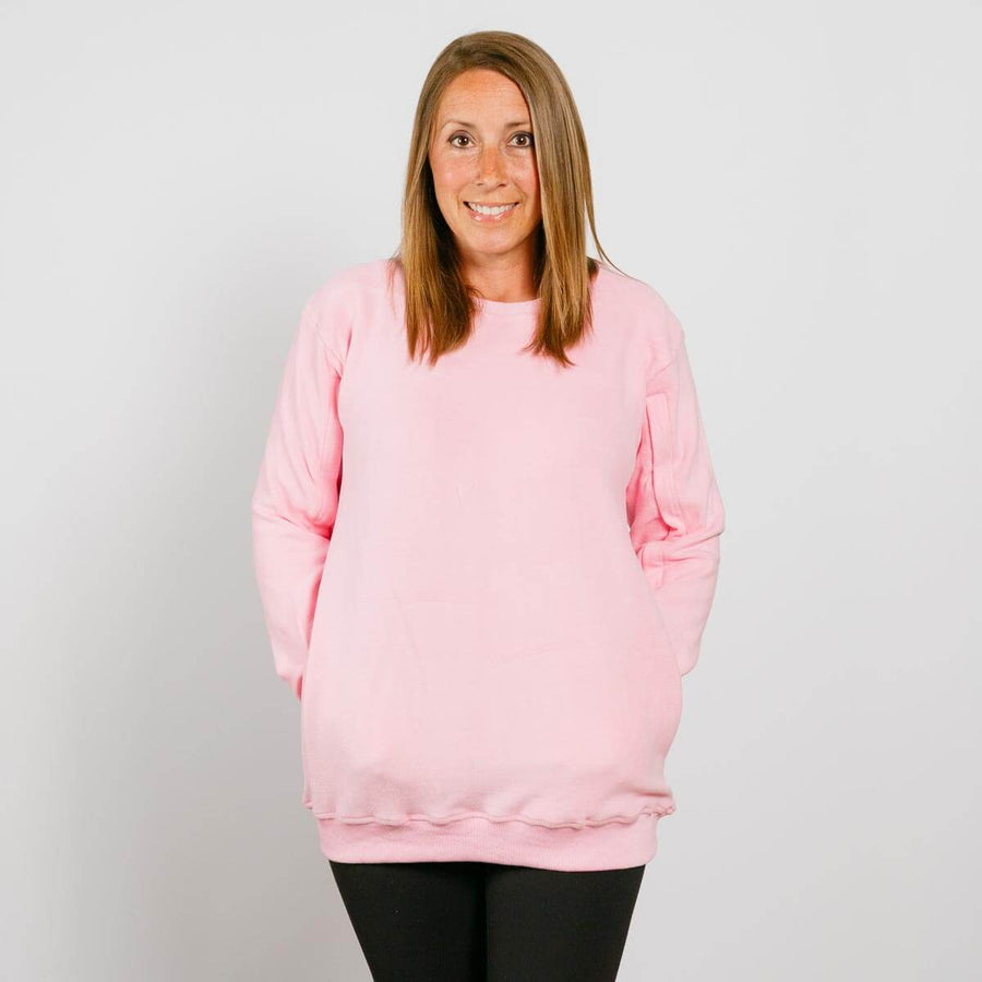 Woman wearing a pink crewneck sweatshirt and black pants, smiling at camera against white background.