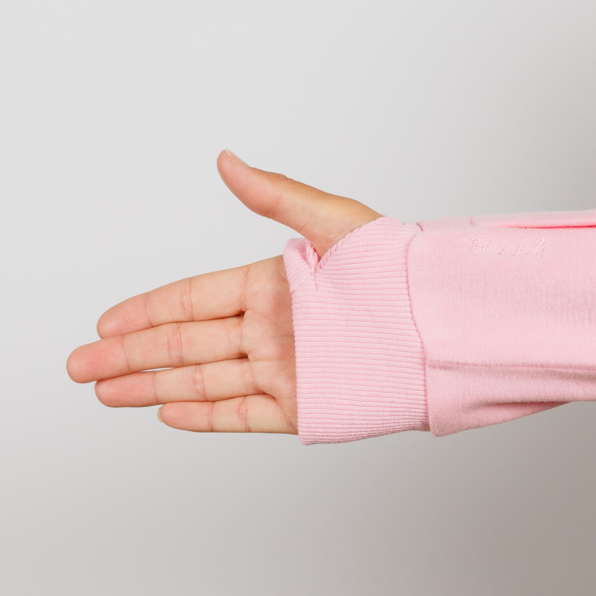 Child's hand extends from pink ribbed crewneck sleeve against neutral gray background.