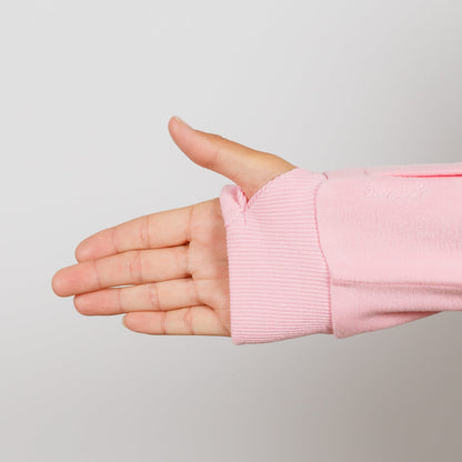 Child's hand extends from pink ribbed crewneck sleeve against neutral gray background.