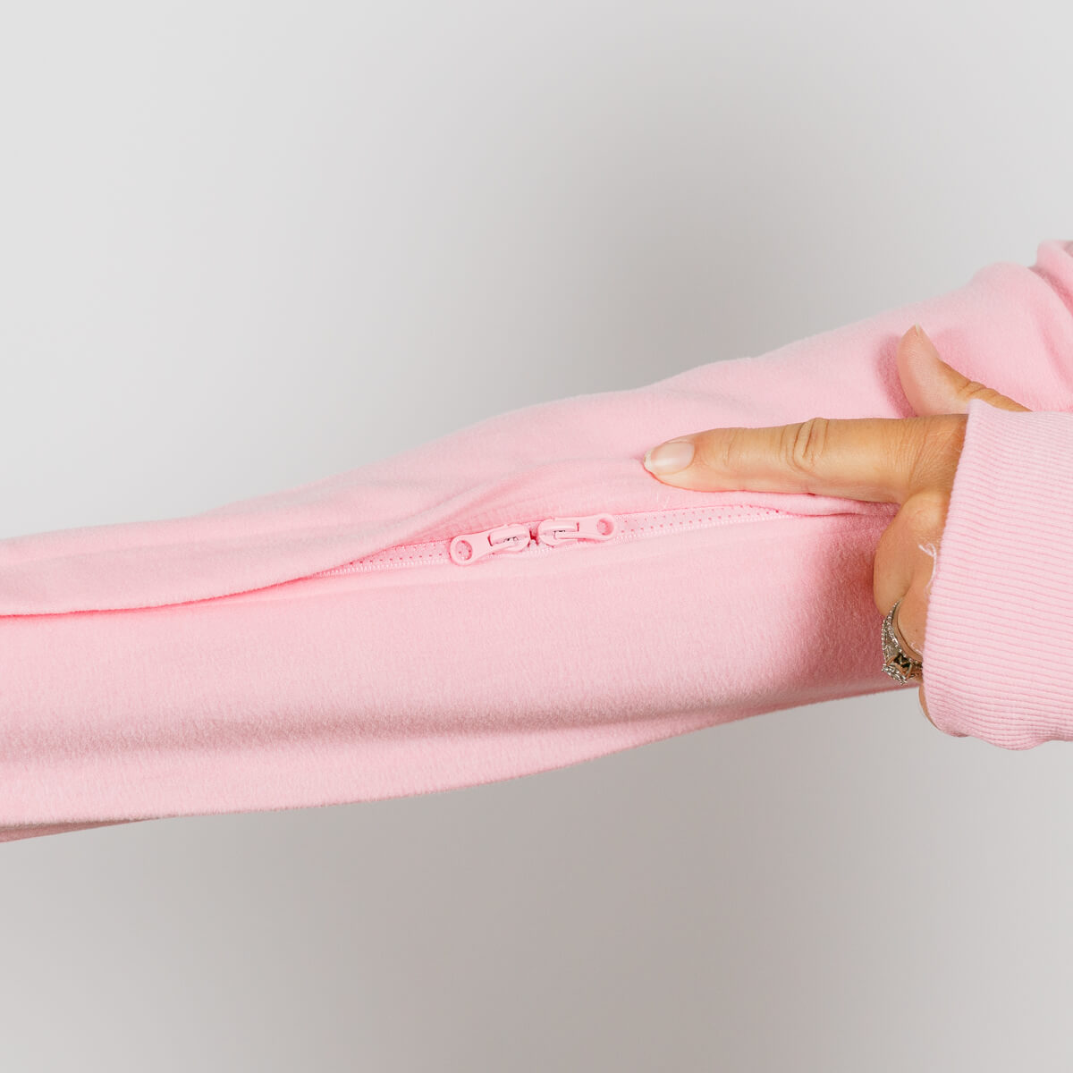 Hand holding open a pink crewneck sweatshirt to display an interior zipper pocket detail.