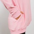 Pink crewneck sweatshirt showing kangaroo pocket detail with striped fabric visible through opening.