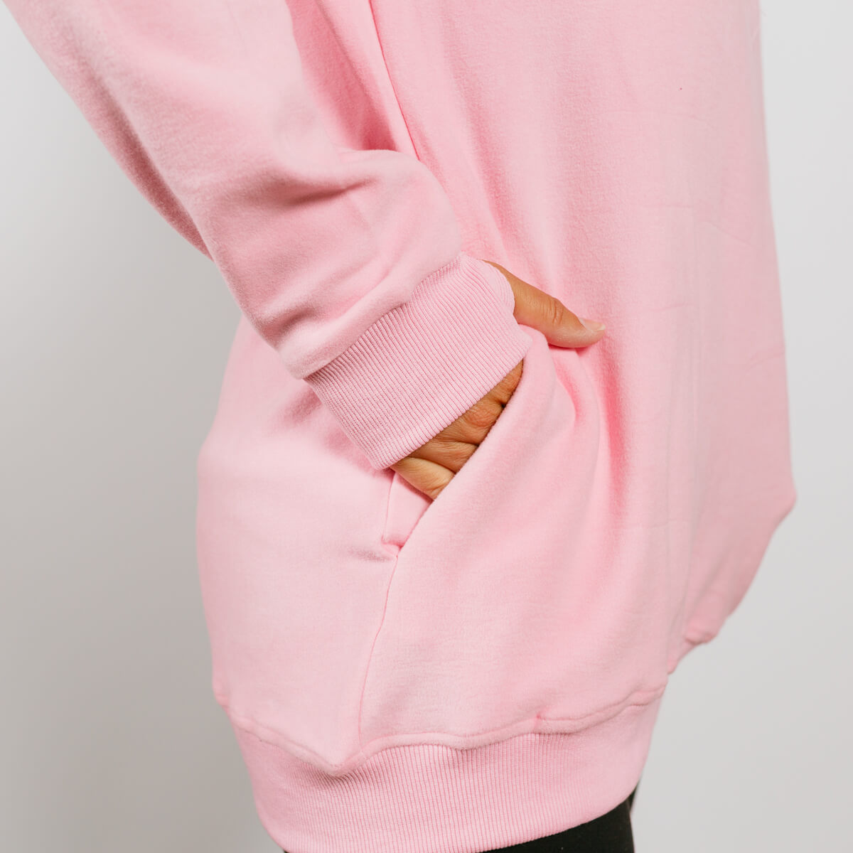 Pink crewneck sweatshirt showing kangaroo pocket detail with striped fabric visible through opening.