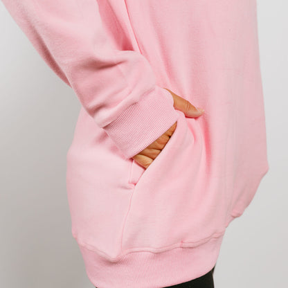 Pink crewneck sweatshirt showing kangaroo pocket detail with striped fabric visible through opening.
