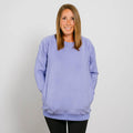 Woman wearing a light purple crewneck sweatshirt with hands in pockets, smiling at camera.