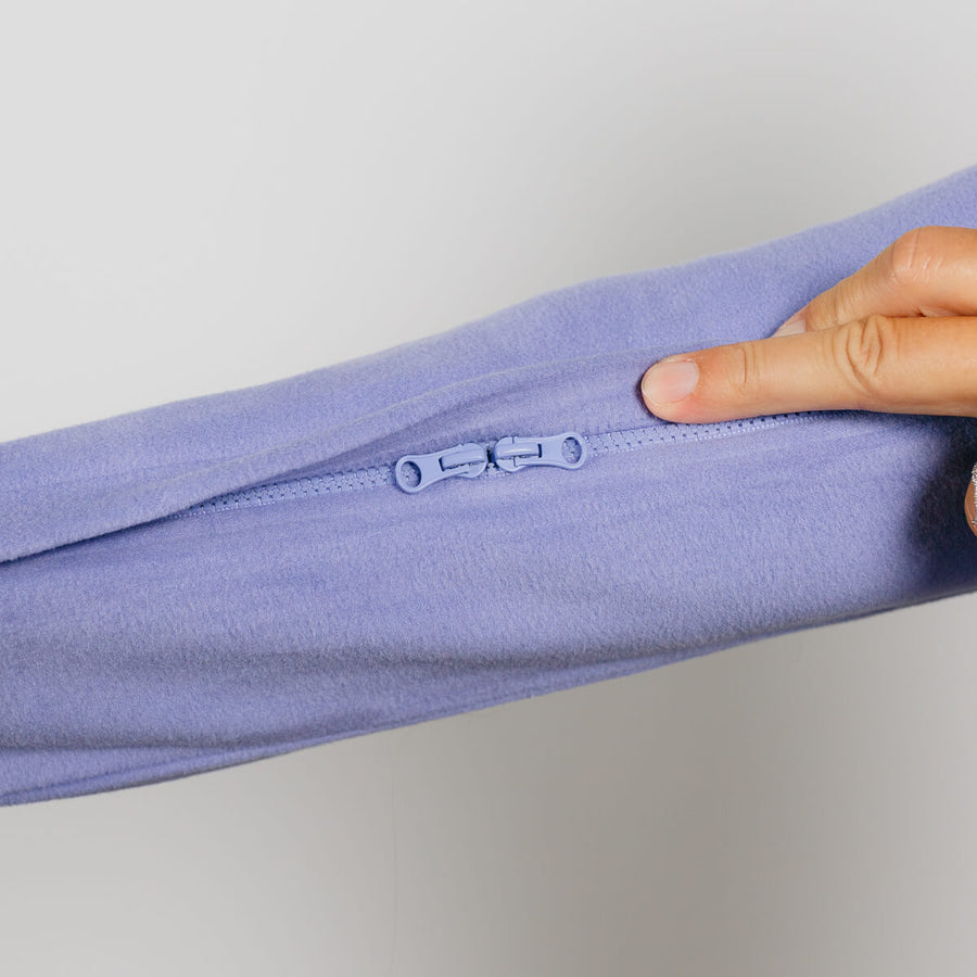 Hand pointing to a small zipper detail on a light purple crewneck sweatshirt.