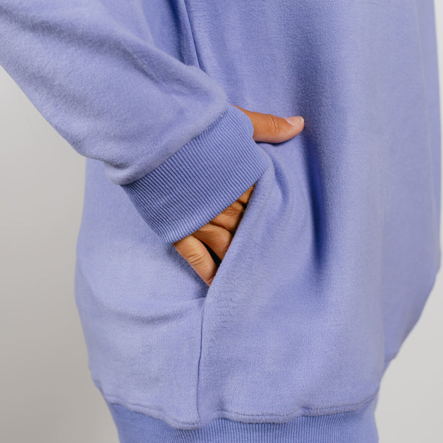 Person's hand resting in a light purple crewneck sweater's front kangaroo pocket.