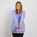 Woman wearing a light purple crewneck sweatshirt with thumb holes and black pants, smiling at camera.