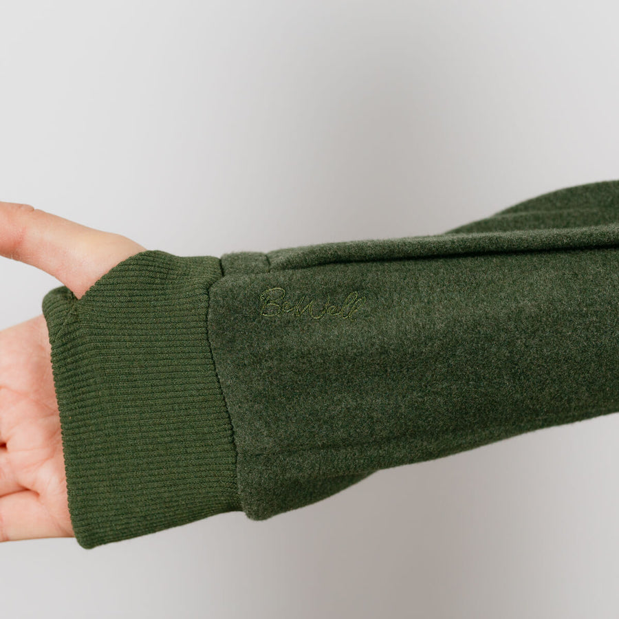 Person wearing olive green IV crewneck, close-up of ribbed cuff and sleeve detail.