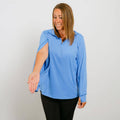 Woman wearing a light blue long-sleeve quarter zip top with black pants, smiling downward.
