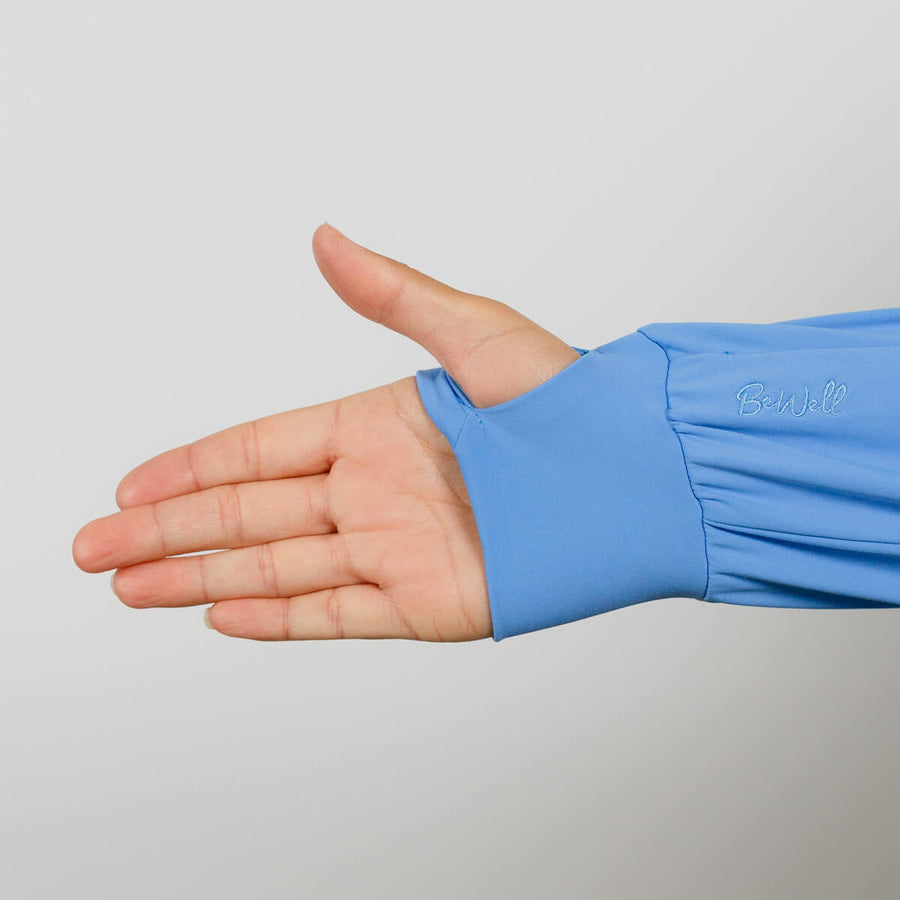 Person wearing a blue quarter zip with hand extended, showing the cuff detail against a gray background.