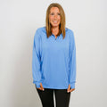 Woman wearing a light blue long-sleeve collared shirt with black pants against a white background.