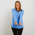Woman wearing blue quarter zip hoodie with orange thumb holes and black pants against white background.