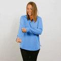 Woman wearing light blue quarter zip pullover and black pants smiles while gesturing with both hands.