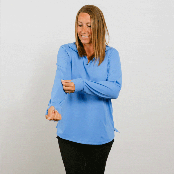 Woman wearing light blue quarter zip pullover and black pants smiles while gesturing with both hands. #gif