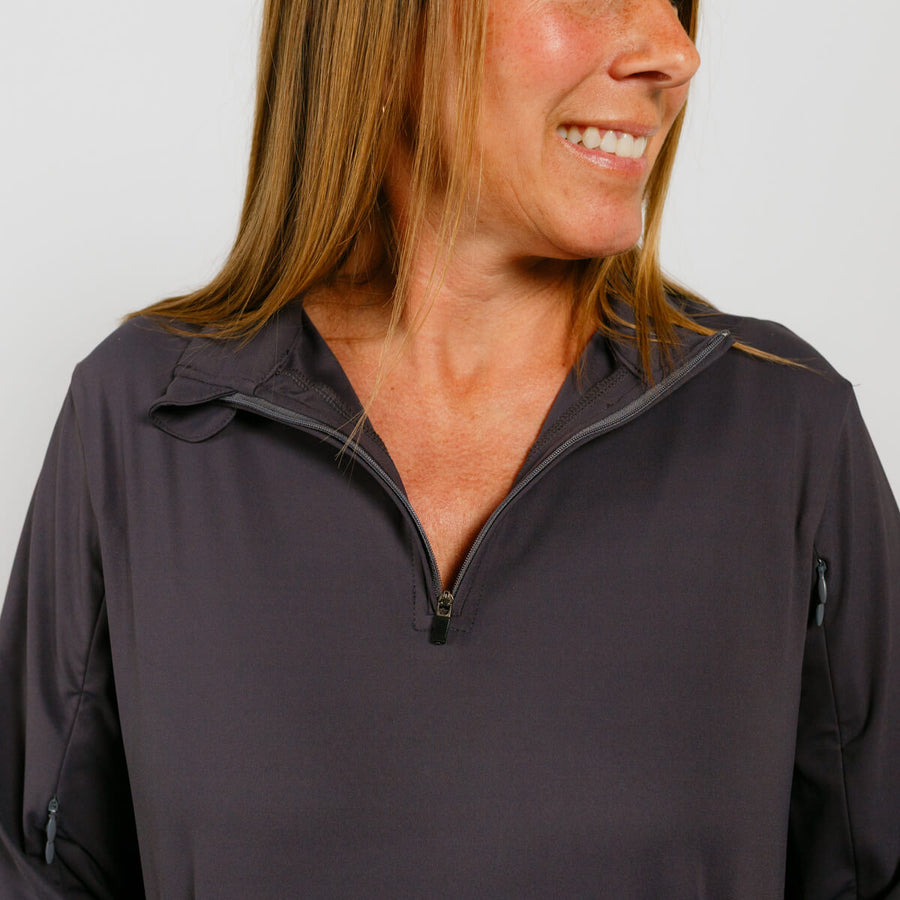 Woman wearing a dark gray quarter-zip pullover smiles while looking to the side.