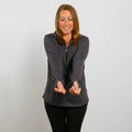 Woman wearing a dark gray quarter zip jacket over black pants, smiling with hands extended forward.