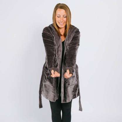 Woman wearing a long gray velvet hooded cardigan over black clothing, smiling downward.
