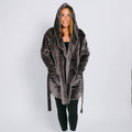 Woman wearing gray velvet hooded robe over black clothing, smiling at camera against white background.
