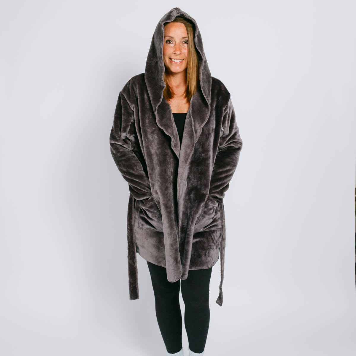 Woman wearing gray velvet hooded robe over black clothing, smiling at camera against white background.