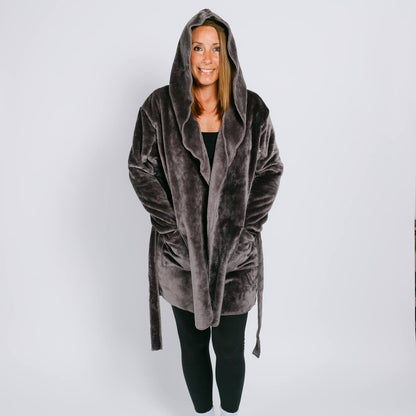 Woman wearing gray velvet hooded robe over black clothing, smiling at camera against white background.