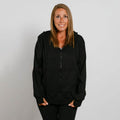 Woman wearing a black zip-up hoodie with her hands in the front pockets, smiling at the camera.