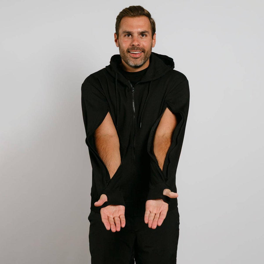 Man wearing black zip hoodie with large cutout holes on the shoulders and thumbholes at wrists.