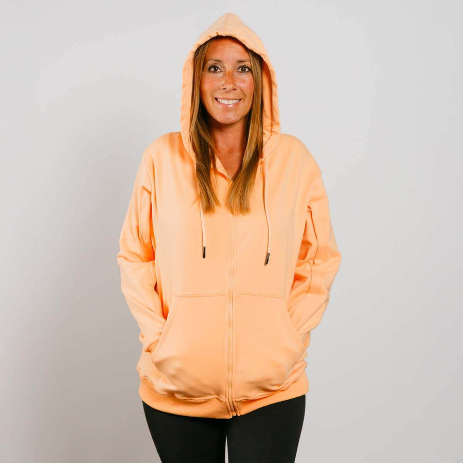 Woman wearing peach IV zip hoodie with hood up, front view showing full-length fit.