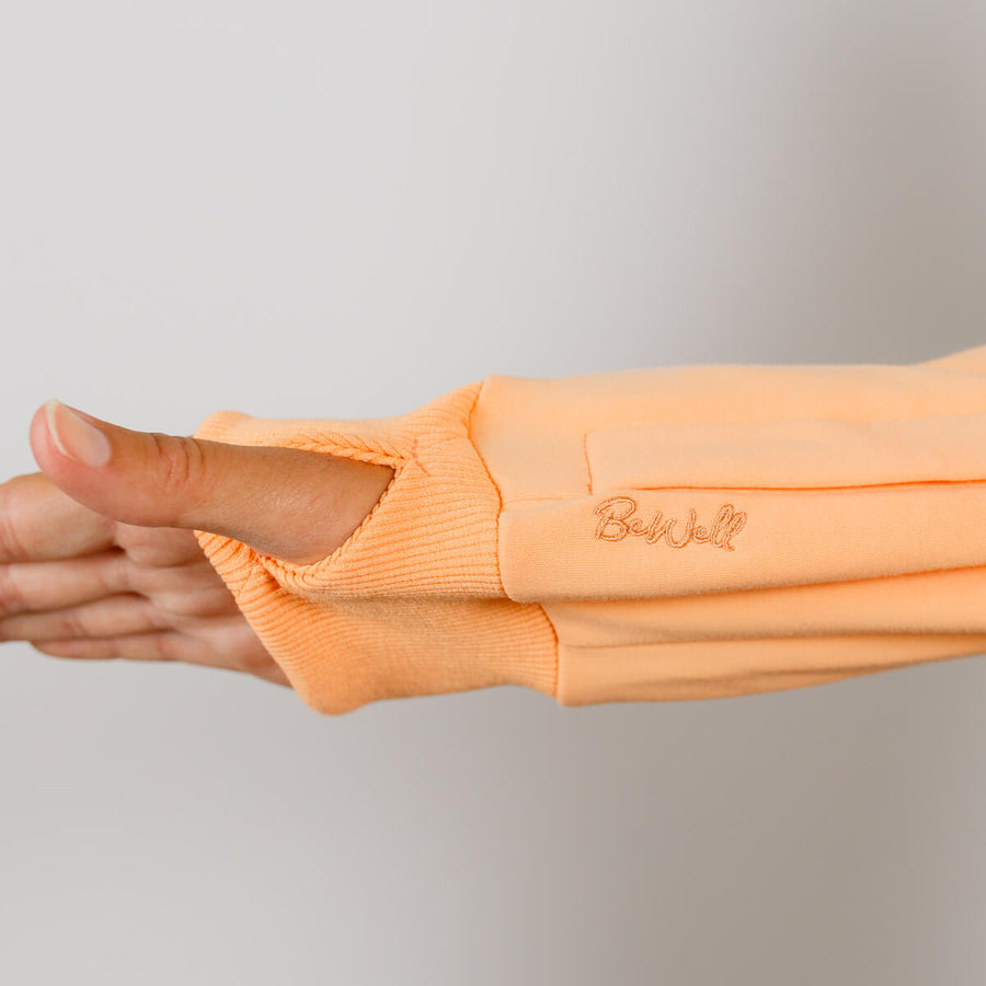 Person wearing peach IV zip hoodie with left sleeve zipper open for medical access.