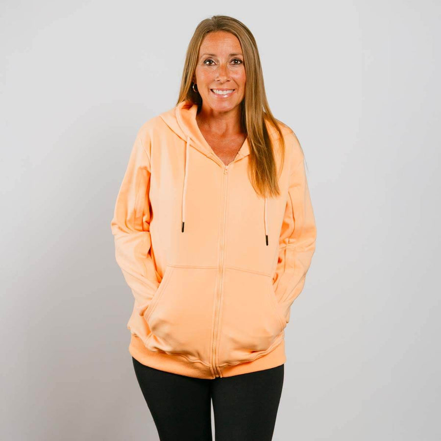 Woman wearing peach IV zip hoodie with front zipper, standing against white background.