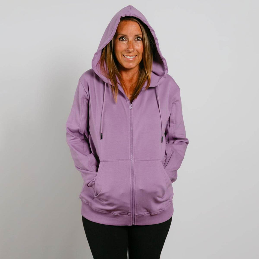 Woman wearing a lavender zip-up hoodie with hood down, smiling at camera against white background.