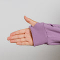 Child's hand extended from purple zip hoodie with ribbed cuff against gray background.