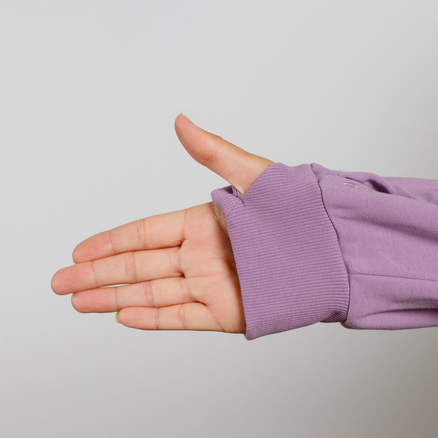 Child's hand extended from purple zip hoodie with ribbed cuff against gray background.