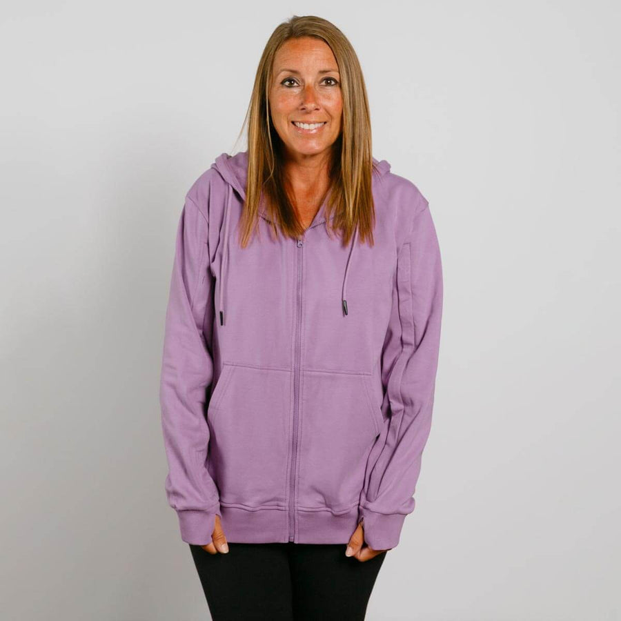 Woman wearing a lavender zip-up hoodie over black pants, smiling at camera.