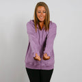 Woman wearing a purple zip hoodie with kangaroo pocket and black pants, smiling downward.