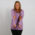 Woman wearing lavender zip-up hoodie with thumb holes and black pants, smiling downward.