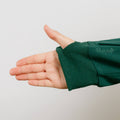 A person's arm extends from a dark green zip hoodie with ribbed cuffs against a light gray background.