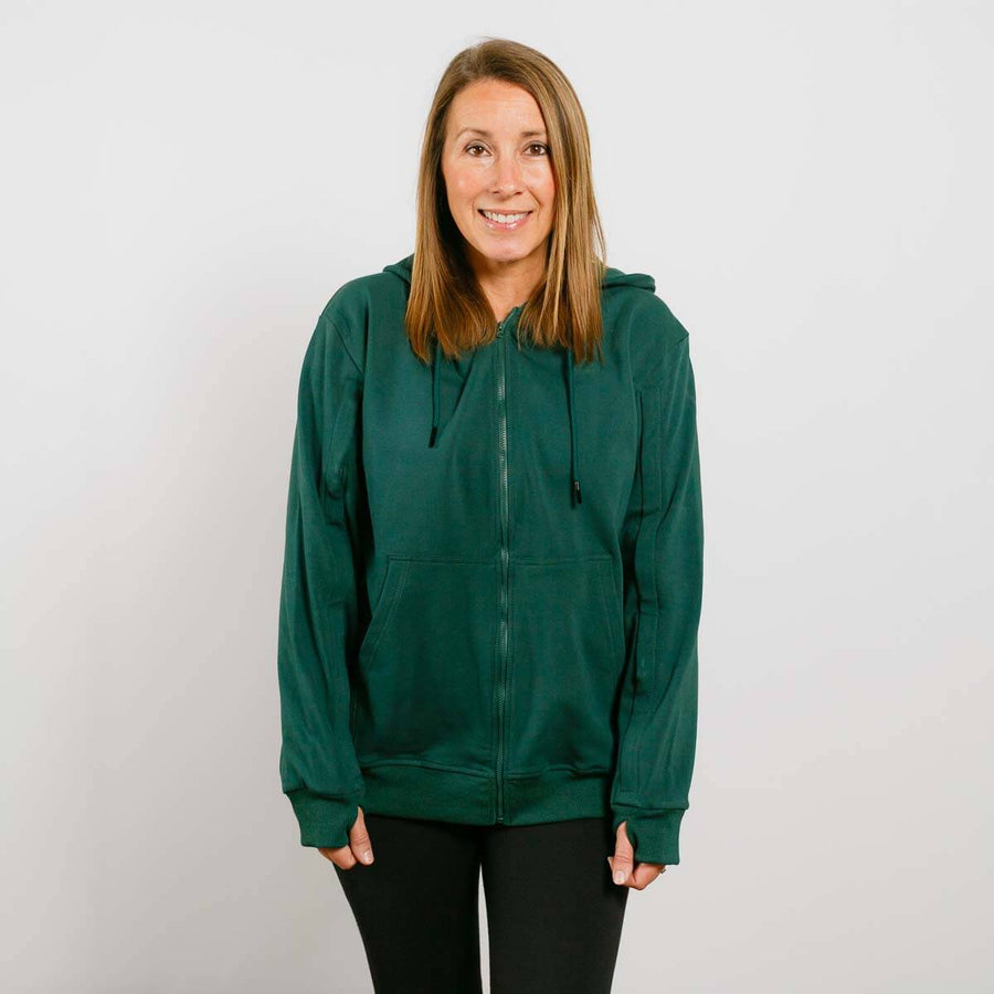 Woman wearing a dark green zip-up hoodie and black pants, smiling at camera.