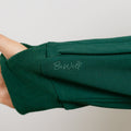 Person wearing a dark green zip hoodie with ribbed cuffs and embroidered text on the sleeve.