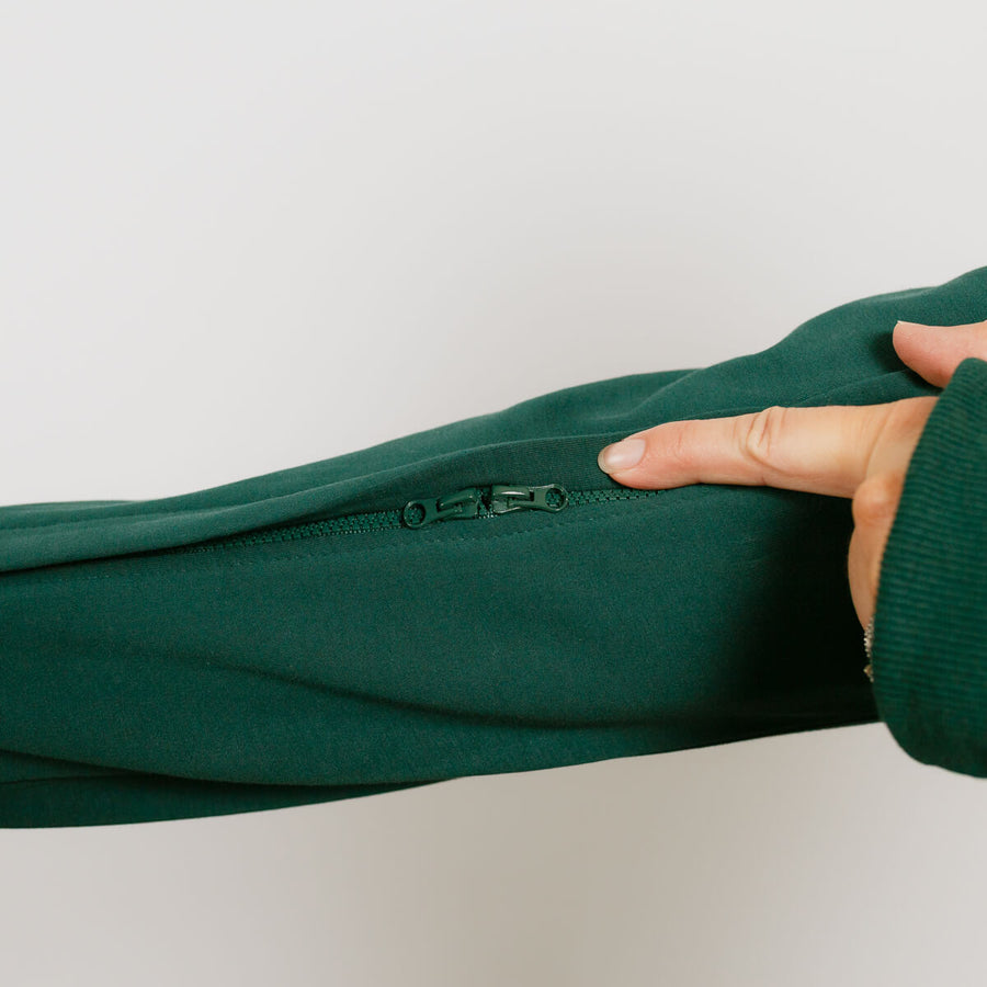 Hand holding open dark green zip hoodie to display interior zipper detail and fabric texture.